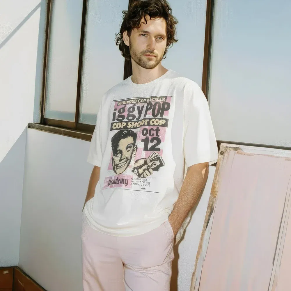 Unisex oversized off-white t-shirt made from 100% premium cotton. This tee features a vintage-style graphic designed to look like a punk rock concert poster for an 'Iggy Pop' event. The design includes bold typography, a stylized portrait, and event details, creating an authentic retro look perfect for fans of music history and punk-inspired fashion